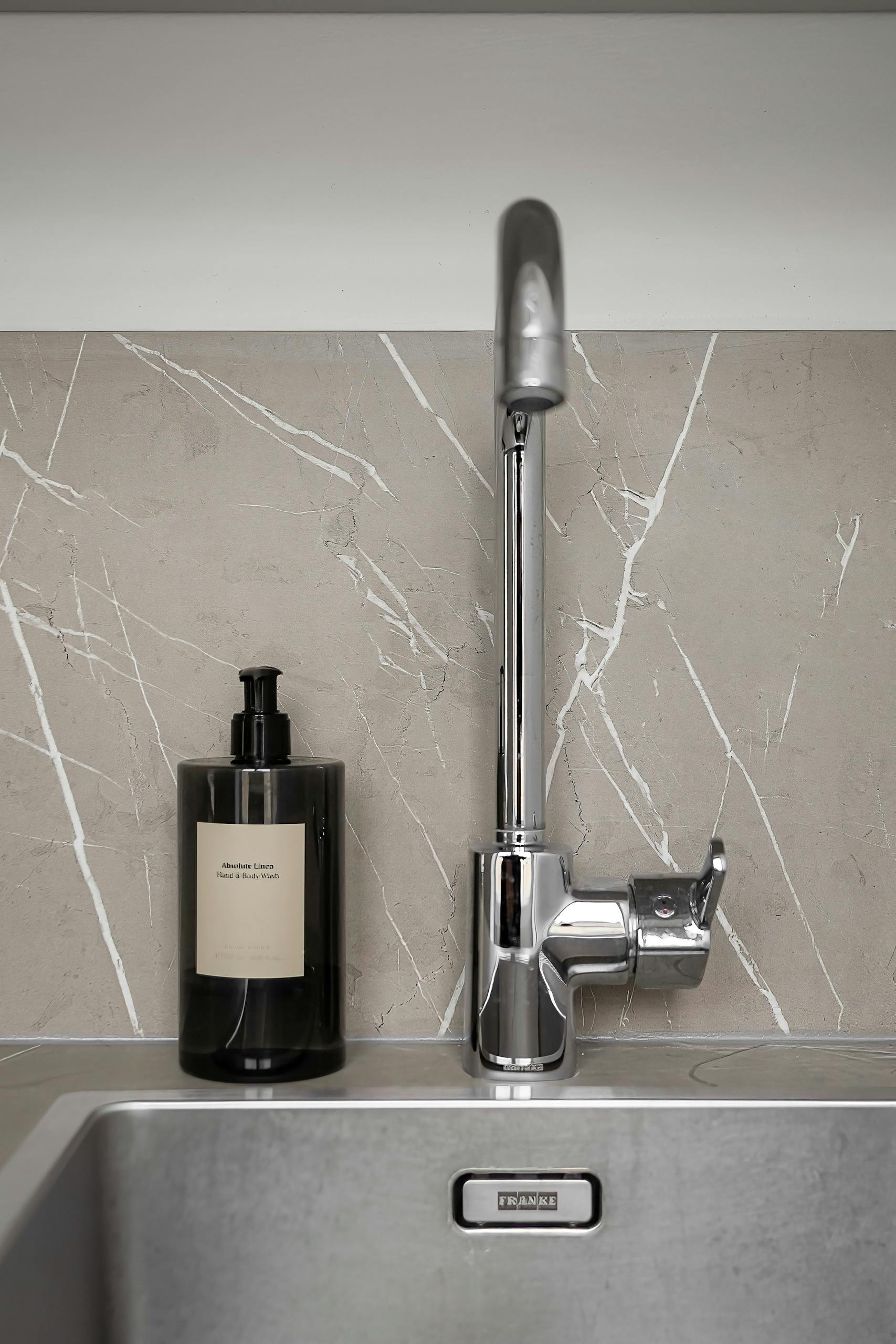 A sleek modern kitchen sink with dish soap set against a minimalist backdrop.