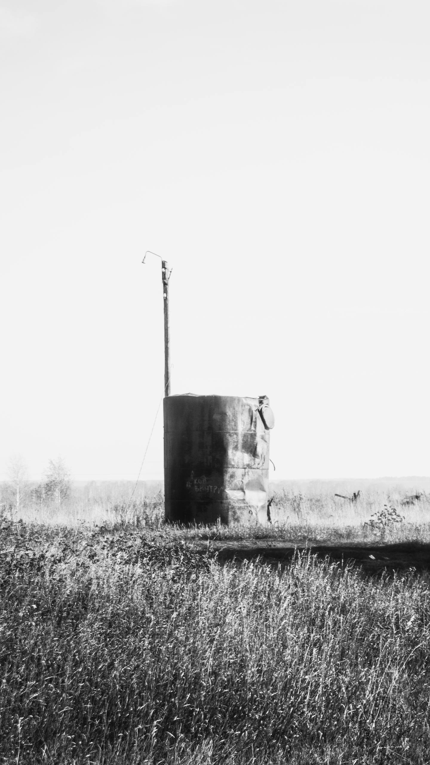 Black and white photo of an abandoned water tower in a rural field against a clear sky.