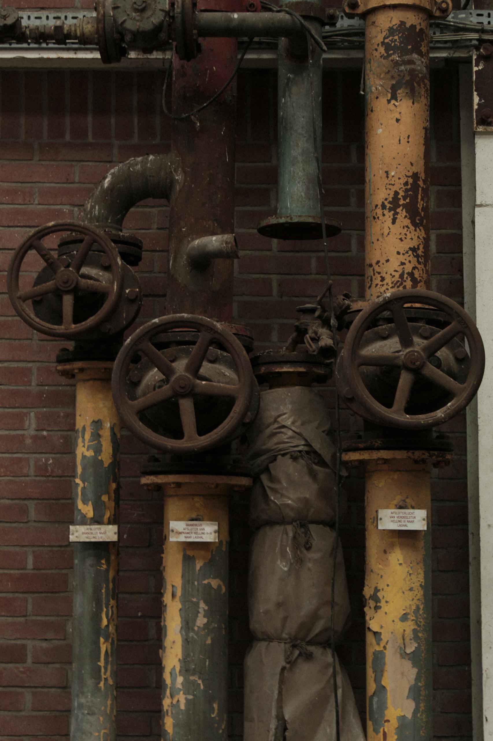 Close-up of rusty valves and pipes set against a brick wall, showcasing industrial decay.